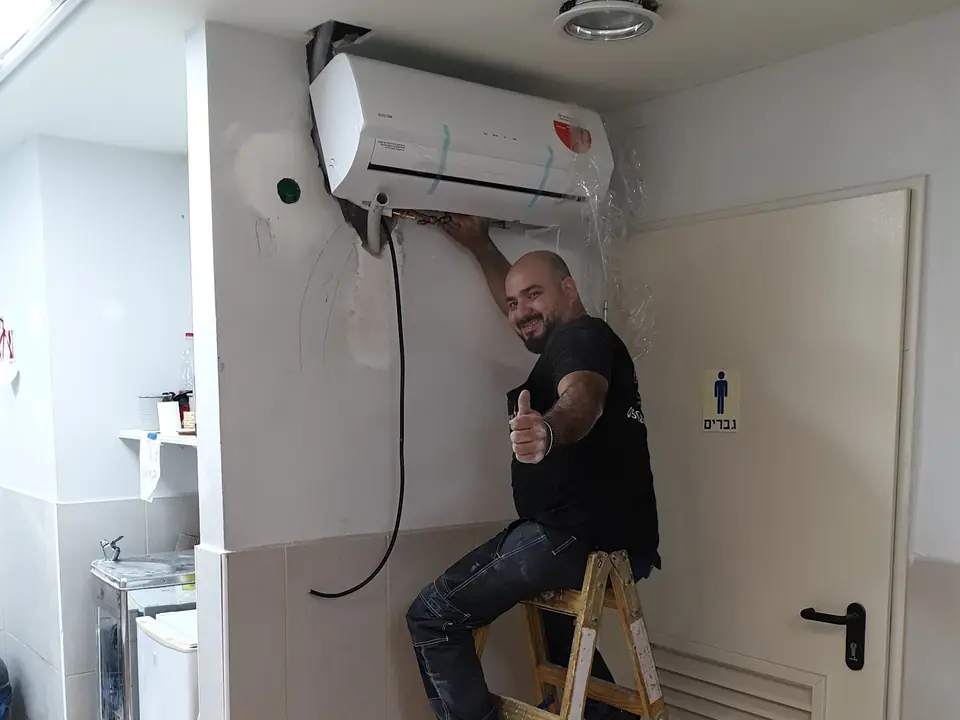 טכנאי על סולם מתקין מזגן עילי על קיר לבן